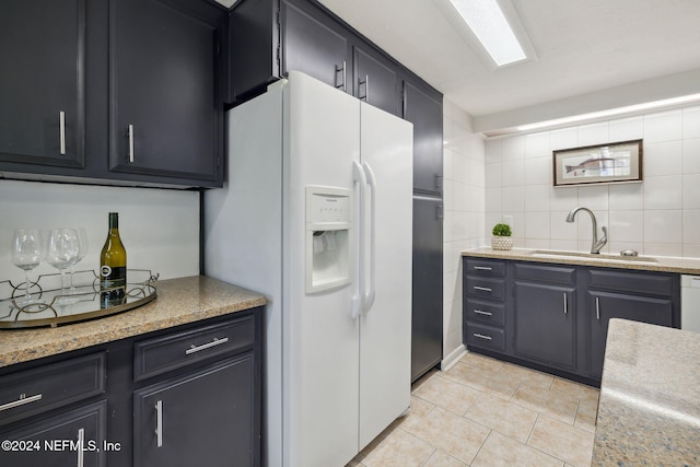 kitchen featuring sink, decorative backsplash, light stone countertops, white fridge with ice dispenser, and light tile patterned floors