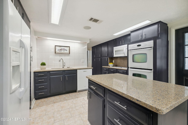 kitchen featuring white appliances, sink, light stone countertops, tasteful backsplash, and a kitchen island