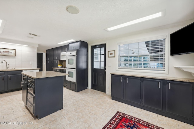 kitchen featuring a center island, sink, a textured ceiling, white appliances, and decorative backsplash