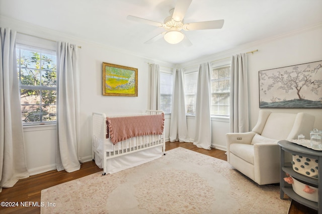 bedroom featuring ceiling fan, crown molding, a nursery area, and hardwood / wood-style flooring