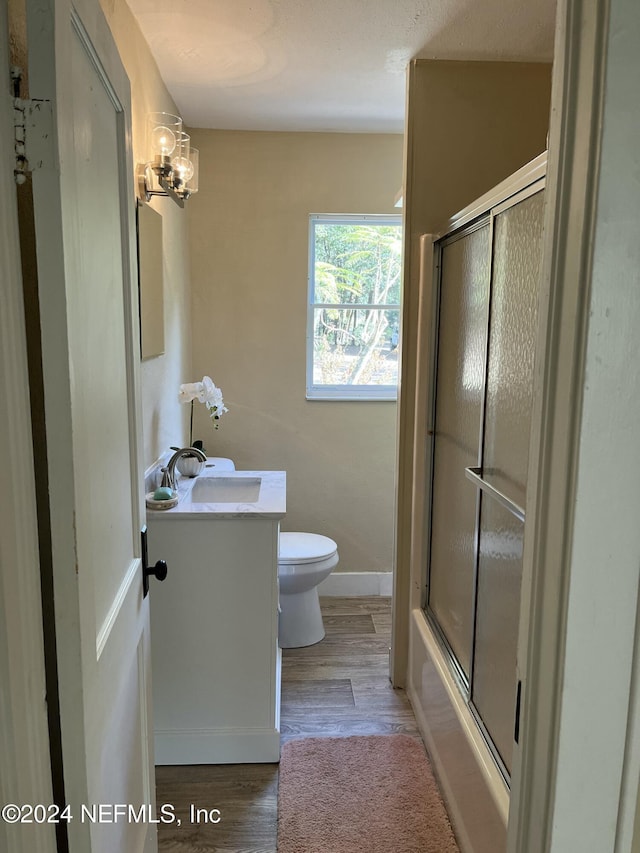 full bathroom with an inviting chandelier, bath / shower combo with glass door, wood-type flooring, toilet, and vanity