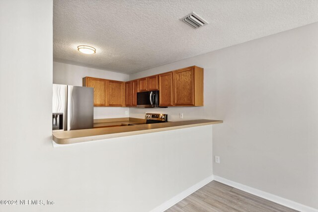 kitchen featuring kitchen peninsula, stainless steel appliances, a textured ceiling, and light wood-type flooring