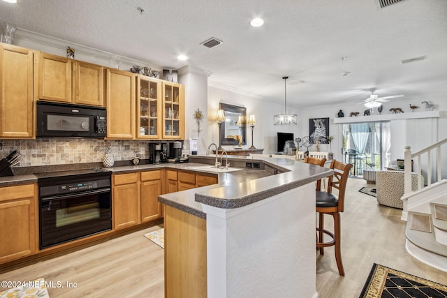 kitchen with black appliances, a kitchen breakfast bar, crown molding, hanging light fixtures, and light hardwood / wood-style flooring