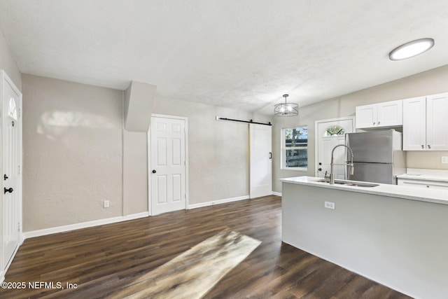 kitchen with white cabinetry, sink, a barn door, stainless steel fridge, and pendant lighting