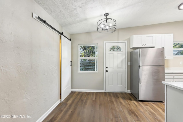 kitchen featuring white cabinets, a barn door, a wealth of natural light, decorative light fixtures, and stainless steel refrigerator