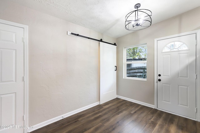 entryway with a textured ceiling, a barn door, dark hardwood / wood-style floors, and a notable chandelier