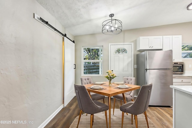 dining room featuring a barn door, light hardwood / wood-style floors, a textured ceiling, and a wealth of natural light