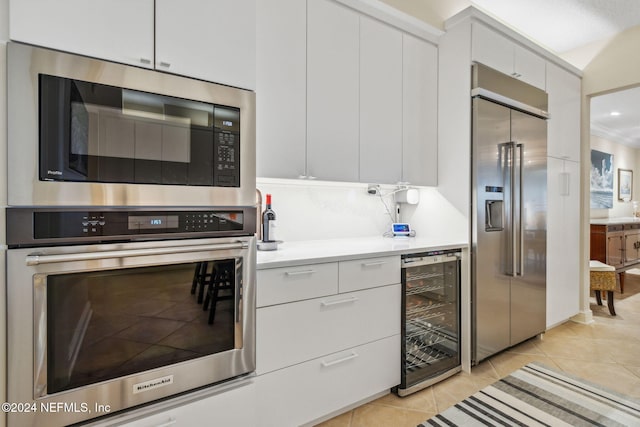 kitchen featuring light tile patterned floors, built in appliances, white cabinetry, and wine cooler