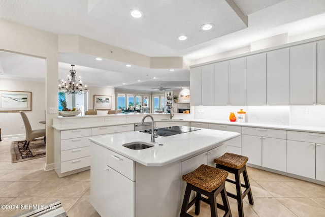 kitchen featuring kitchen peninsula, a breakfast bar, a kitchen island with sink, sink, and white cabinets