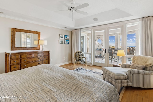 bedroom featuring hardwood / wood-style floors, ceiling fan, access to exterior, and a tray ceiling