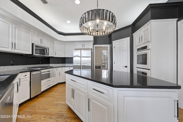 kitchen with appliances with stainless steel finishes, decorative light fixtures, an inviting chandelier, a center island, and white cabinetry