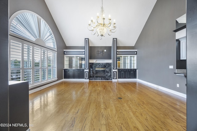 unfurnished living room with hardwood / wood-style floors, a premium fireplace, high vaulted ceiling, and an inviting chandelier