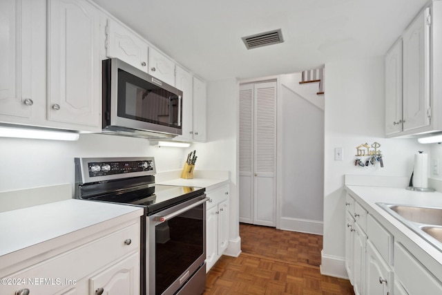 kitchen with white cabinetry, dark parquet floors, sink, and appliances with stainless steel finishes