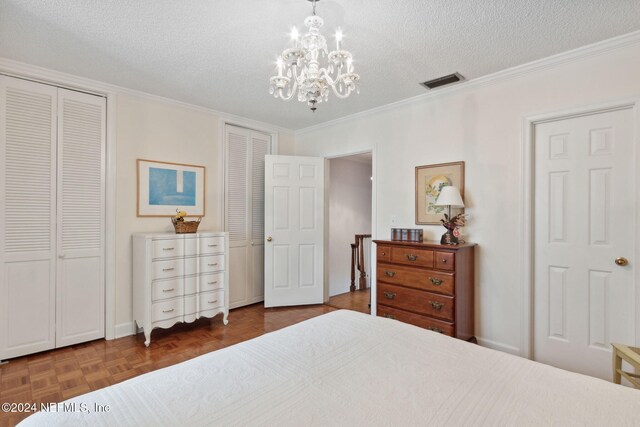 bedroom with dark parquet flooring, ornamental molding, a textured ceiling, a notable chandelier, and multiple closets