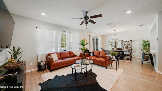 living room with ceiling fan with notable chandelier, light hardwood / wood-style floors, and a textured ceiling