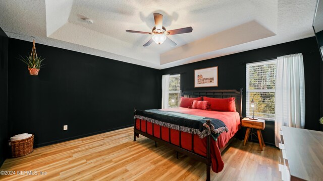 bedroom featuring hardwood / wood-style floors, a raised ceiling, multiple windows, and ceiling fan