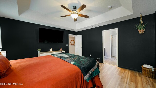 bedroom featuring ceiling fan, light hardwood / wood-style floors, a textured ceiling, and a tray ceiling