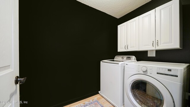 laundry area with washer and dryer, cabinets, a textured ceiling, and light wood-type flooring