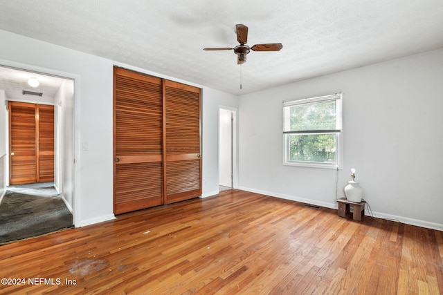 unfurnished bedroom with a textured ceiling, light hardwood / wood-style floors, a closet, and ceiling fan