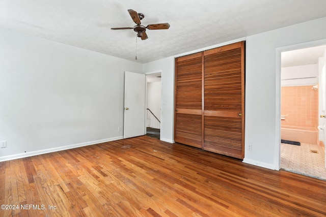 unfurnished bedroom featuring ensuite bathroom, a textured ceiling, ceiling fan, hardwood / wood-style floors, and a closet