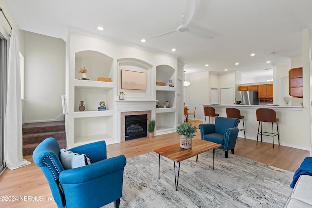 living room with a tile fireplace, light hardwood / wood-style floors, built in features, and ceiling fan