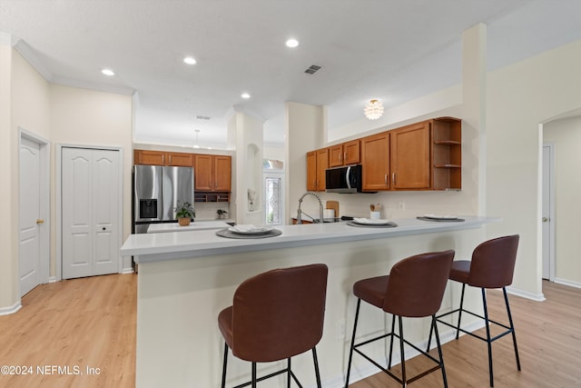 kitchen with sink, kitchen peninsula, light hardwood / wood-style floors, a breakfast bar, and appliances with stainless steel finishes