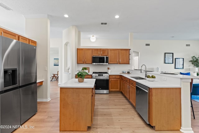 kitchen featuring kitchen peninsula, appliances with stainless steel finishes, sink, light hardwood / wood-style floors, and a kitchen island