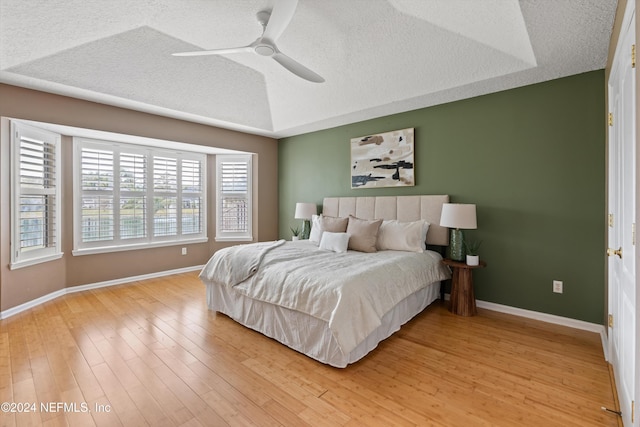 bedroom with a raised ceiling, ceiling fan, light hardwood / wood-style floors, and a textured ceiling