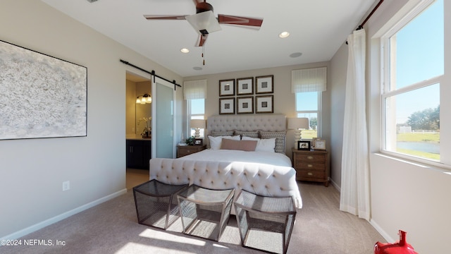 carpeted bedroom featuring a barn door, ensuite bath, and ceiling fan