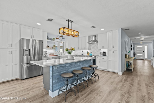 kitchen with decorative light fixtures, white cabinets, stainless steel appliances, and wall chimney range hood