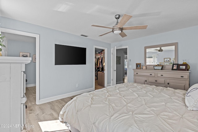 bedroom with ceiling fan, a fireplace, a walk in closet, a closet, and light wood-type flooring