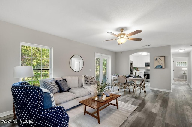 living room with a wealth of natural light, dark wood-type flooring, and ceiling fan