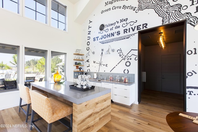 kitchen featuring backsplash, a high ceiling, sink, light hardwood / wood-style flooring, and white cabinetry