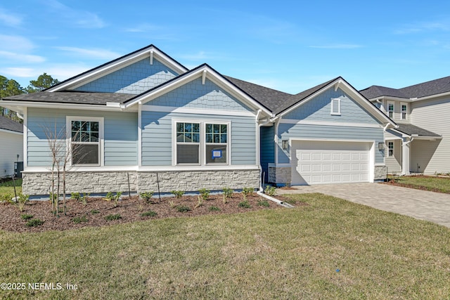 craftsman-style house featuring an attached garage, a shingled roof, stone siding, decorative driveway, and a front lawn