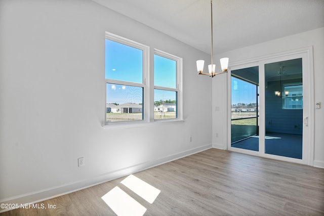 spare room with baseboards, a notable chandelier, and light wood finished floors