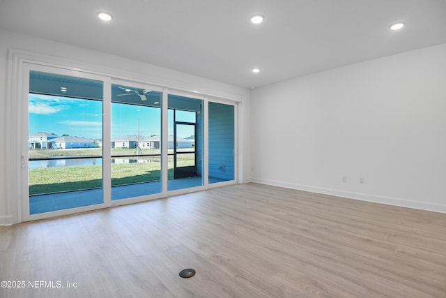 empty room featuring baseboards, ceiling fan, a water view, light wood-style floors, and recessed lighting