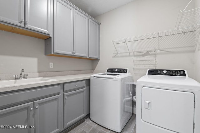 laundry area with washing machine and clothes dryer, light hardwood / wood-style floors, cabinets, and sink