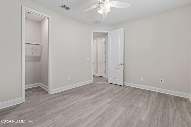 unfurnished bedroom with a closet, light hardwood / wood-style floors, a spacious closet, and ceiling fan