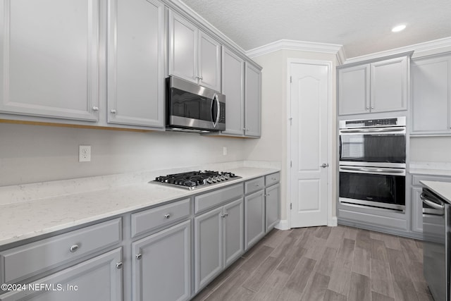 kitchen with appliances with stainless steel finishes, ornamental molding, a textured ceiling, gray cabinets, and light hardwood / wood-style floors