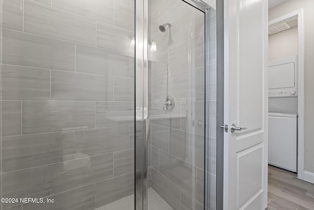 bathroom featuring hardwood / wood-style floors, a shower with shower door, and stacked washing maching and dryer