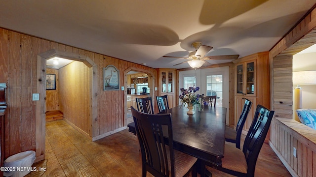 dining space with wooden walls, french doors, ceiling fan, and light hardwood / wood-style flooring