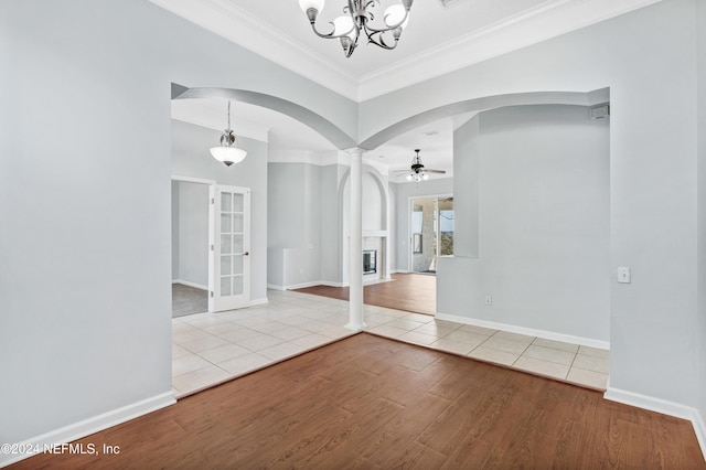 empty room featuring ornate columns, ornamental molding, ceiling fan with notable chandelier, and light wood-type flooring