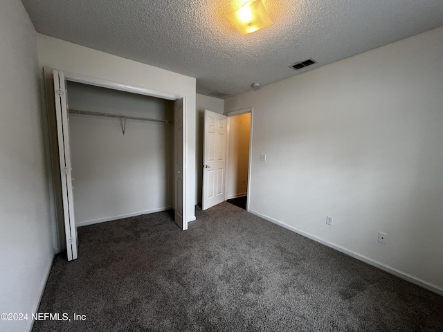 unfurnished bedroom featuring dark carpet, a textured ceiling, and a closet