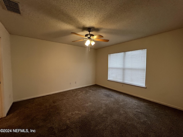 empty room featuring ceiling fan, a textured ceiling, and dark colored carpet