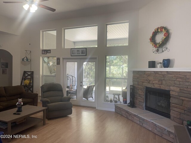 living room with french doors, light wood-type flooring, ceiling fan, a fireplace, and a high ceiling