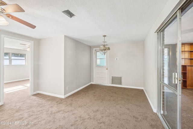 spare room featuring light carpet, a textured ceiling, and ceiling fan with notable chandelier