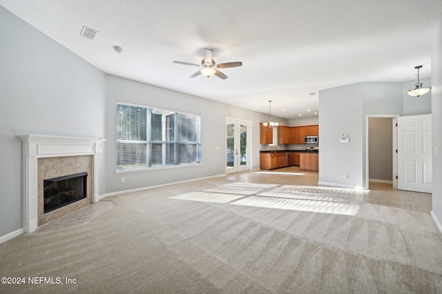 unfurnished living room with light carpet, french doors, ceiling fan with notable chandelier, a textured ceiling, and a fireplace