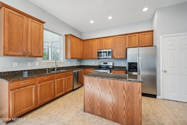 kitchen with sink, a center island, dark stone counters, light tile patterned floors, and appliances with stainless steel finishes