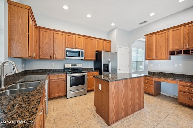 kitchen with dark stone counters, stainless steel appliances, sink, a kitchen island, and light tile patterned flooring