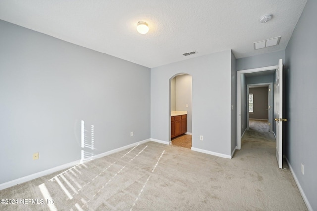 unfurnished bedroom featuring ensuite bath, light colored carpet, and a textured ceiling